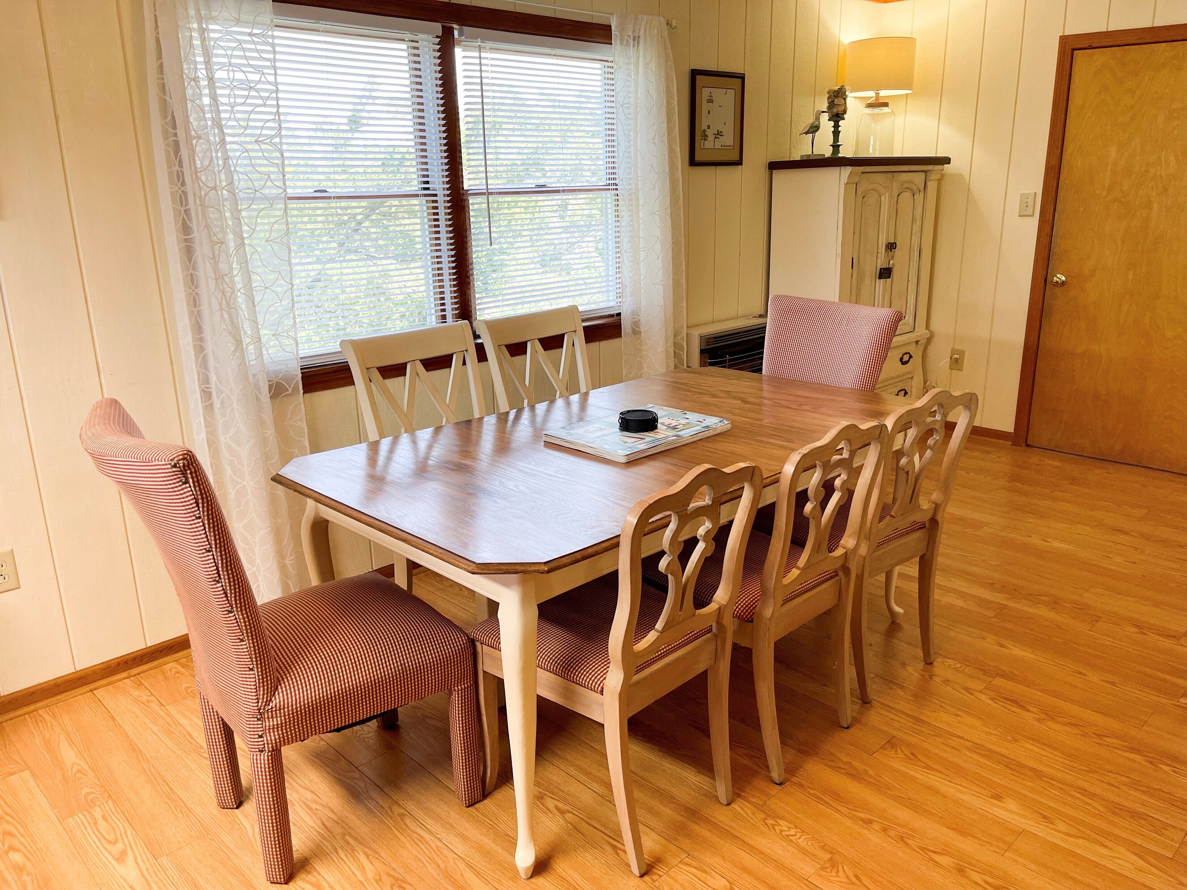 Un comedor con mesa y sillas de madera, una ventana con persianas, una lámpara y una puerta.