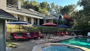 A pool area with lounge chairs and umbrellas, a hot tub, and a brick wall.