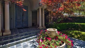 A building entrance with a stone staircase, a blue door, and a garden with red foliage.