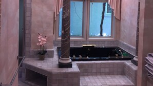 A bathroom with a marble column, a bathtub, and a window with curtains.