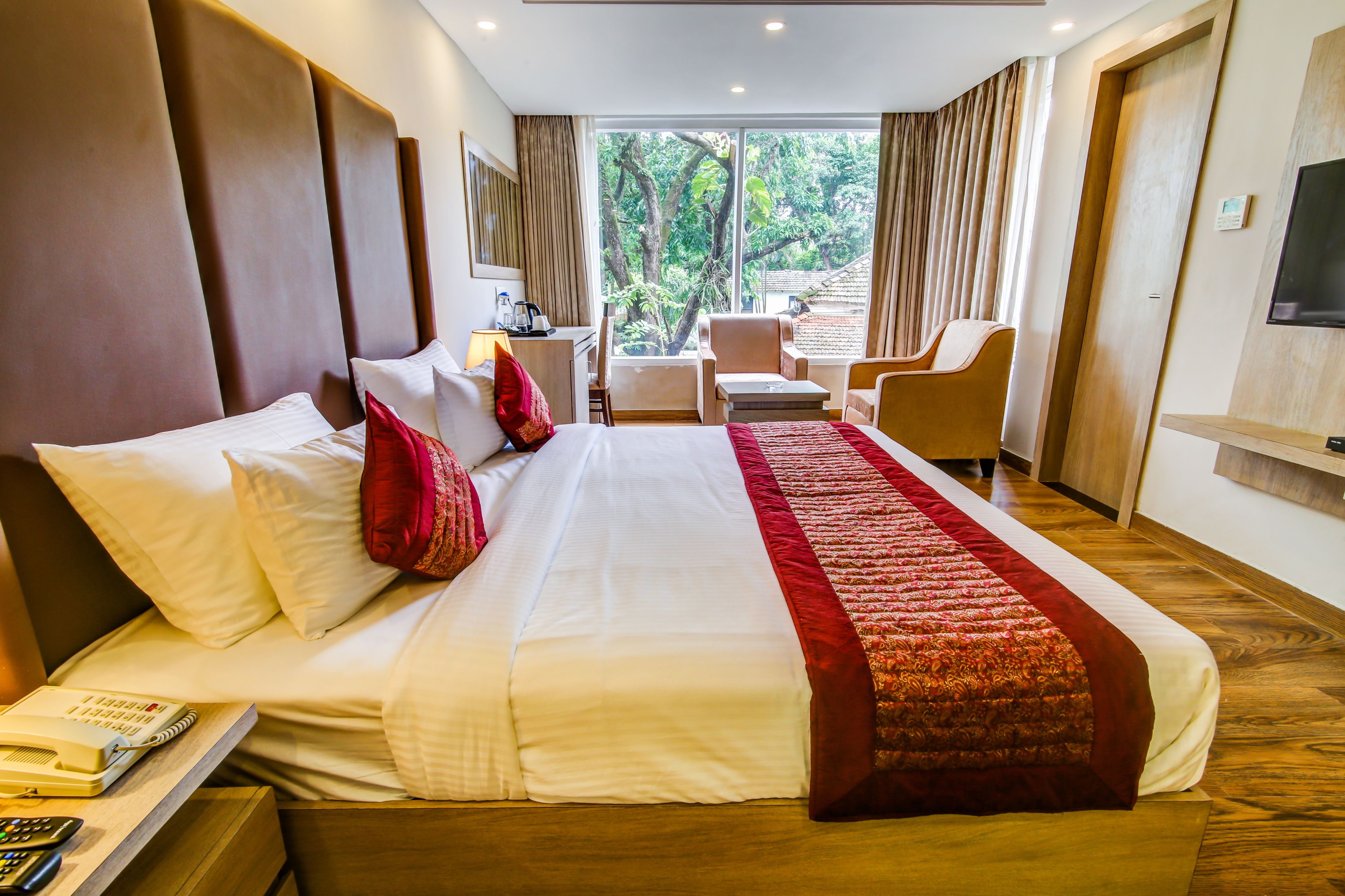 A hotel room with a large bed, a desk with a chair, a small table, and a TV mounted on the wall.