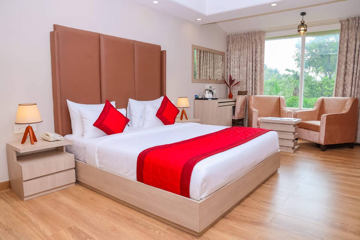 Habitación de hotel con una cama grande, un escritorio, una silla y una ventana con vista a zonas verdes.