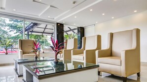 Un vestíbulo moderno con una mesa de centro de vidrio, sillones beige y vistas al exterior.