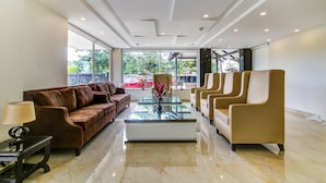 Un hall moderno con un sofá de cuero marrón, sillones beige y una mesa de centro de vidrio, además de una lámpara.