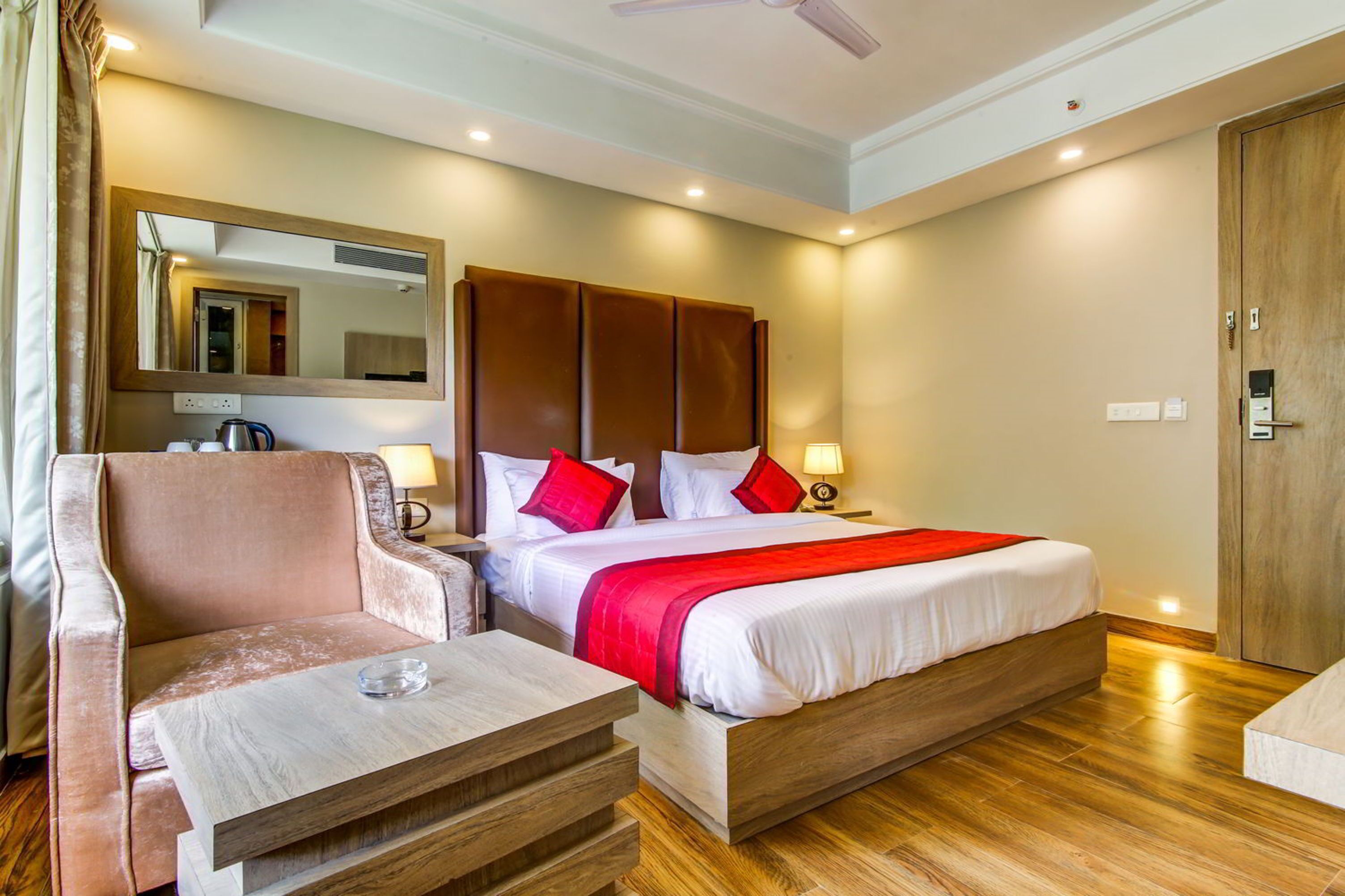 A hotel room with a bed, a sofa, a coffee table, a mirror, and a wardrobe.