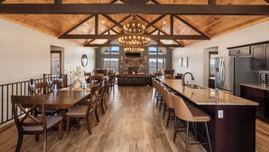 Een ruime keuken met een centraal eiland, een eethoek met houten tafels en stoelen, en een hoge plafond met zichtbare balken.