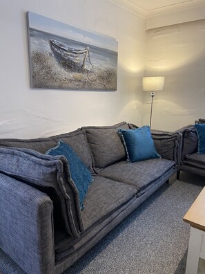 Una sala de estar moderna con un sofá gris, cojines azules, un cuadro de un barco en la pared y una lámpara de pie.
