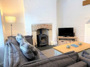 A cozy living room with a fireplace, a sofa, a television, and a table with decorative items. - Triple Deck Cottage 2 mins from Mevagissey Harbour (St Austell)