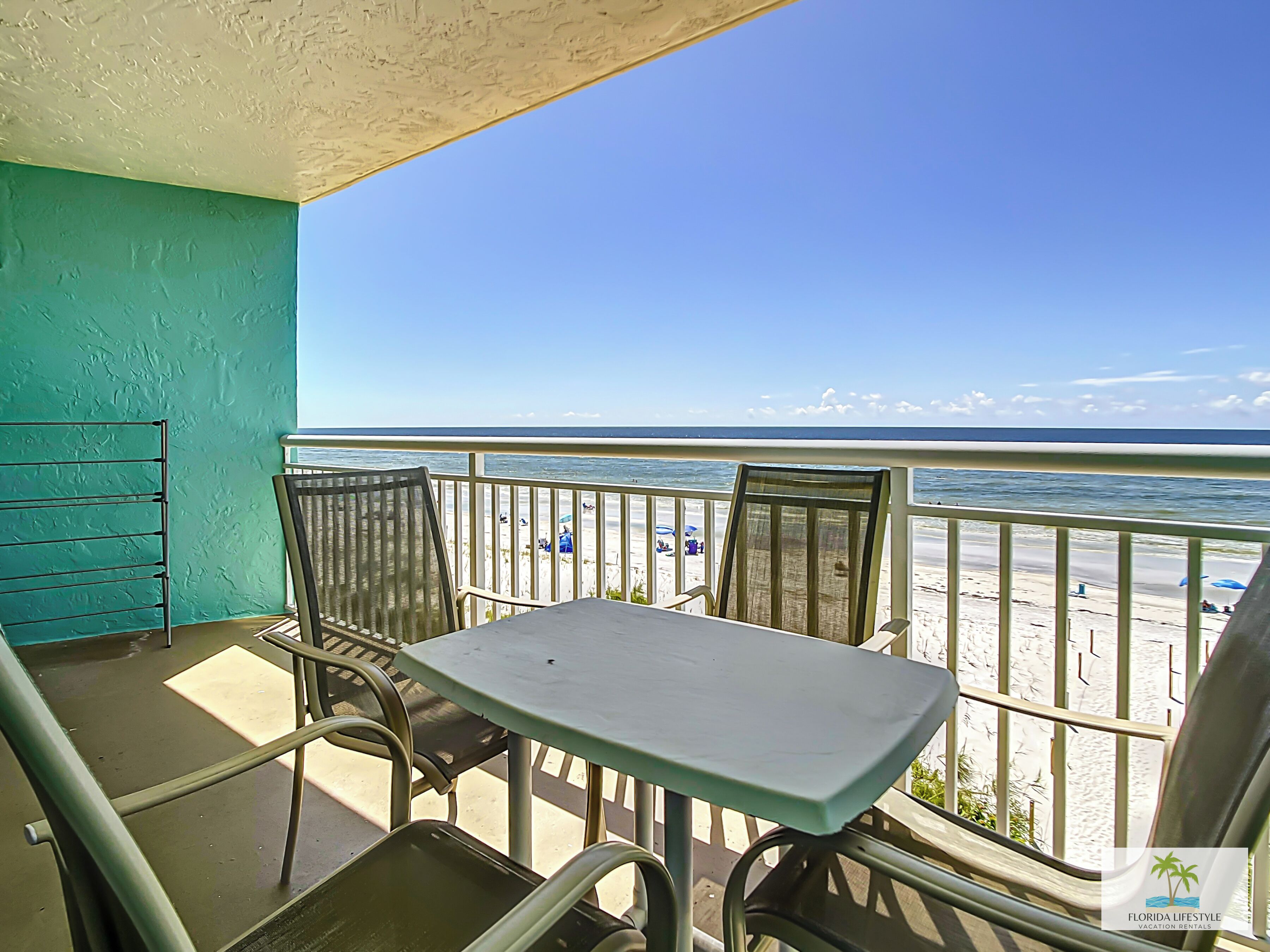 Ein Balkon mit Tisch und Stühlen mit Blick auf einen Strand mit Sonnenschirmen und Personen.