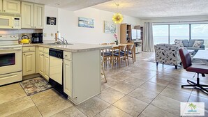 Eine moderne Küche mit Kochinsel, Essbereich mit Stühlen und Wohnbereich mit Sofa und Fernseher.