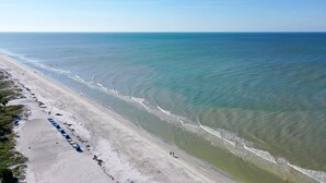 Ein Strand mit einer weiten Sandfläche, einigen Spaziergängern und einer Reihe blauer Sonnenschirme.