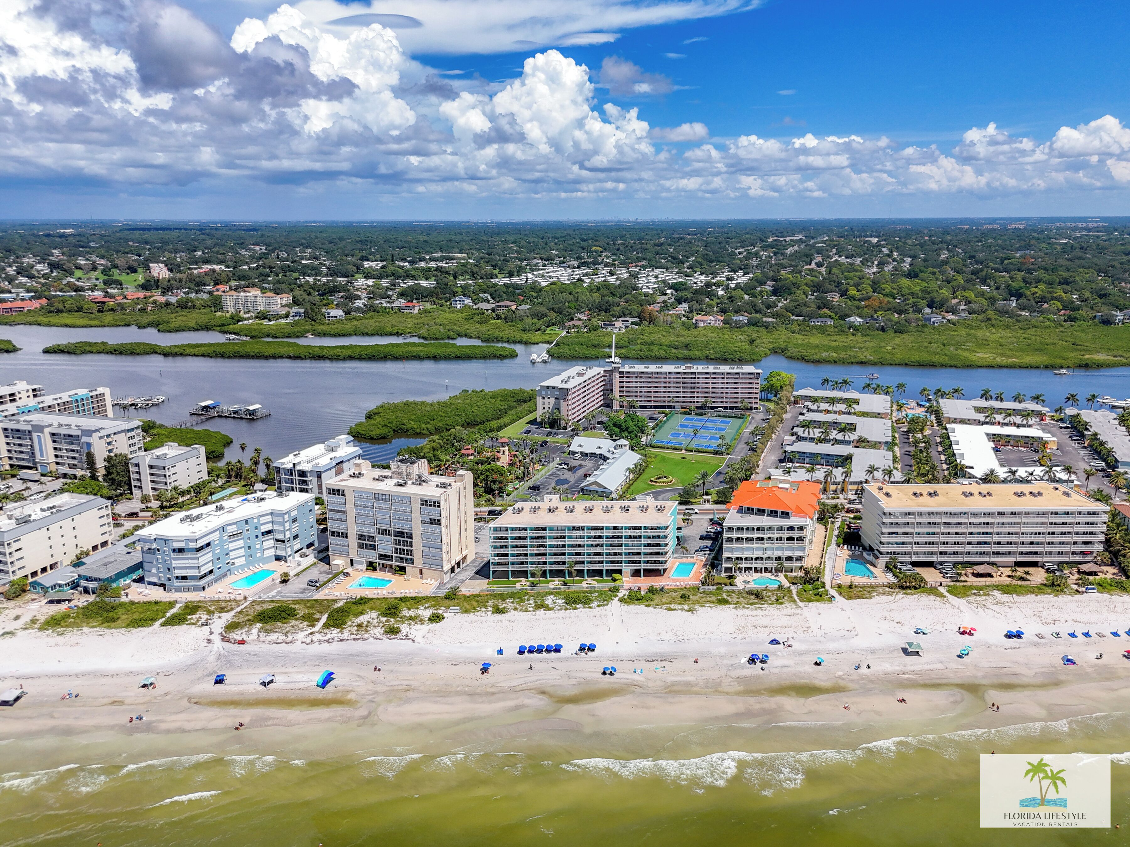 Un hotel frente al mar con varias construcciones, una playa y un puerto deportivo.