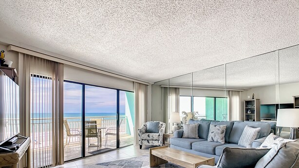 Ein geräumiges Wohnzimmer mit einer großen Couch, einem Couchtisch und einem Fernseher. Ein Balkon bietet Blick aufs Meer.
