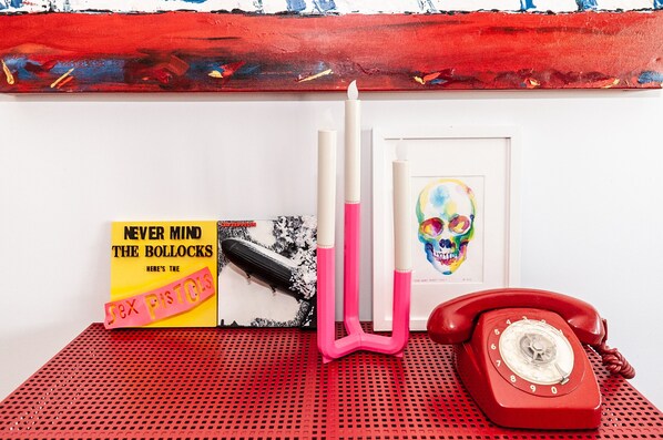 Un téléphone rouge, un livre intitulé « NEVER MIND THE BOLLOCKS », et une photo encadrée d’un crâne coloré sur un fond rouge perforé.