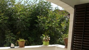 A balcony with a table covered in a blue and white tablecloth, surrounded by white chairs. There are potted plants on the balcony. - Apartments Magda - Two Bedroom Apartment with Terrace and Garden View (Supetar)