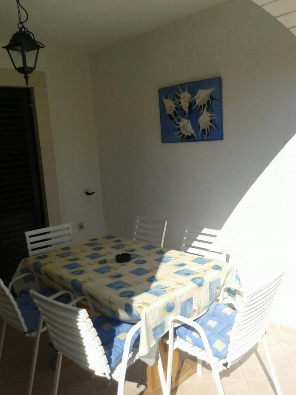 A dining area with a table covered in a blue and white patterned tablecloth, surrounded by white chairs.
