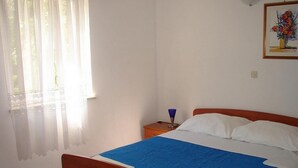 A bedroom with a bed, a nightstand, a lamp, and a window with curtains. - Apartments Magda - Two Bedroom Apartment with Terrace and Garden View (Supetar)