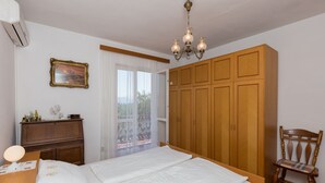Un dormitorio con cama, armario de madera, una silla, escritorio con lámpara y un cuadro en la pared.
