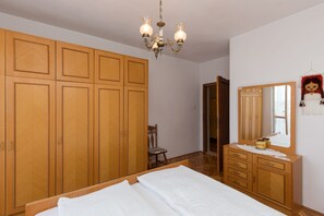 Une chambre à coucher avec des meubles en bois, un lustre, un miroir et une porte donnant sur une autre pièce.