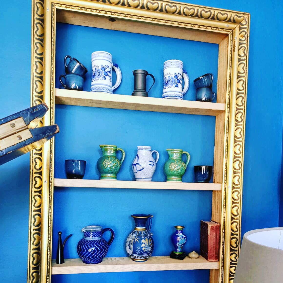 A display of ceramic vases on shelves against a blue wall, framed by an ornate golden frame.