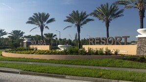 Entrada de un resort con palmeras, un letrero grande que dice "Solara Resort" y una zona de jardín bien cuidada.