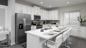 Una cocina moderna con gabinetes blancos, electrodomésticos de acero inoxidable y una isla central con asientos.