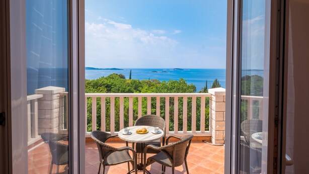 Un balcó amb taula i cadires, amb vista a un paisatge mar i vegetació.