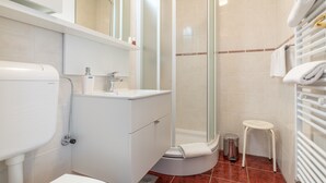 Un bany modern amb vàter, rentapel, dutxa i un petit tamboret.