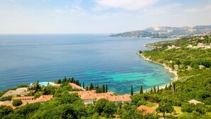 Vista costera amb cel clar, mar turquesa i paisatge amb turons i edificis.