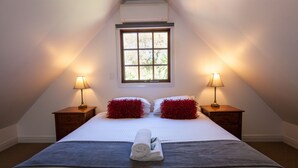 Een netjes opgemaakt bed met een opgerolde handdoek in het midden, twee rode kussens en twee nachtkastjes met lampen.