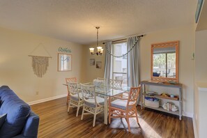 A dining area with a glass table, wicker chairs, a chandelier, and a view of the outdoors. - Lagoon Views & Steps to the Beach/Coligny Plaza! (Hilton Head Island)