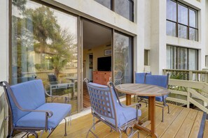 A wooden deck with a round table and two blue chairs, a sliding glass door leading to an interior space, and a white fence in the background. - Lagoon Views & Steps to the Beach/Coligny Plaza! (Hilton Head Island)