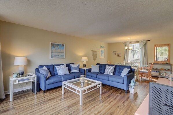 A living room with two blue sofas, a coffee table, and a dining area with a table and chairs. - Lagoon Views & Steps to the Beach/Coligny Plaza! (Hilton Head Island)