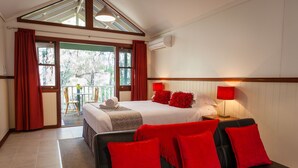 A hotel room with a bed, red pillows, a black sofa, a table with a lamp, and a view of the outdoors. - Cozy Studio Chalet perfect for couples and a veranda overlooking the bushland (Margaret River)