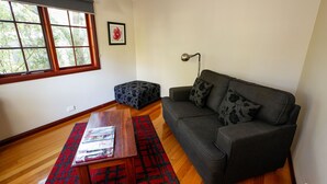 A living room with a dark grey sofa, a wooden coffee table, a red patterned rug, a window with blinds, and a framed picture on the wall.