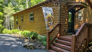 Eine Holzhütte mit einem 'Welcome'-Spruch, einer Holztreppe und einem gepflasterten Einfahrt.