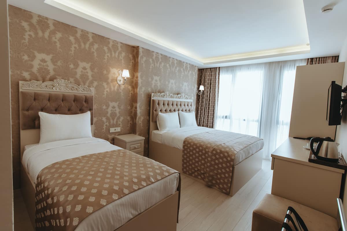 A hotel room with two beds, a desk, a chair, and a television.