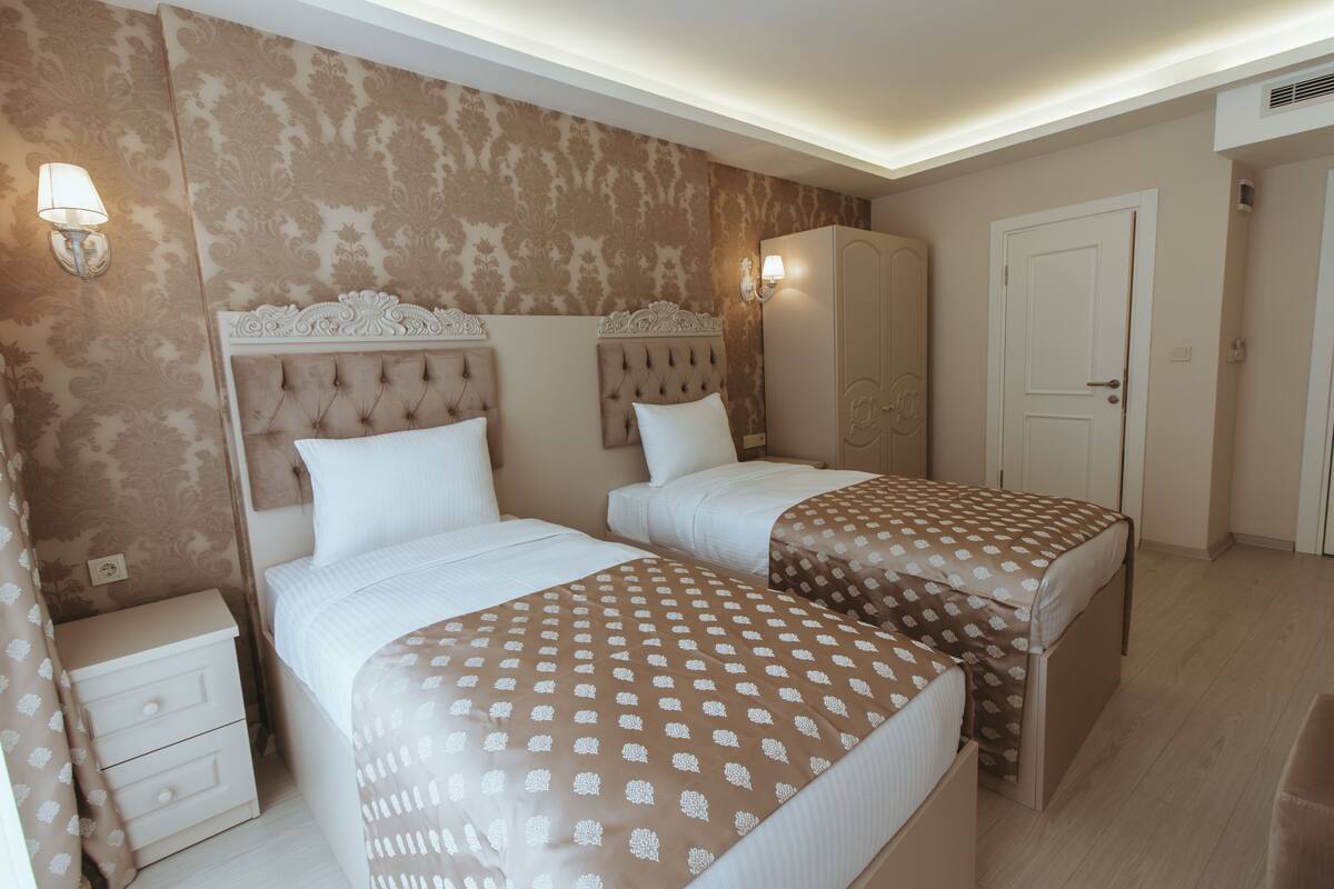A hotel room with two beds, a nightstand, a wardrobe, and a door.