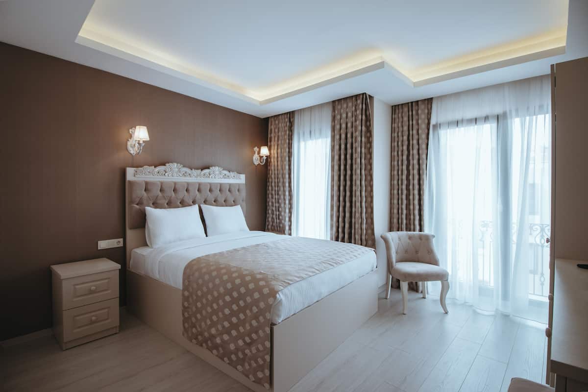 A modern bedroom with a large bed, bedside tables, a chair, and a view of the outdoors through large windows.