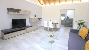 A modern living room with a flat-screen TV, a glass coffee table, and a sofa with a mustard-colored pillow. - Individual house, with 3 bedrooms, 3 bathrooms, living room, kitchen, garden (La Orotava)