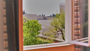 Una habitación con ventana que da a un patio con árboles y un edificio al fondo.