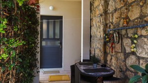Un patio cubierto con un muro de piedra, una puerta negra y una mesa y silla de mimbre.