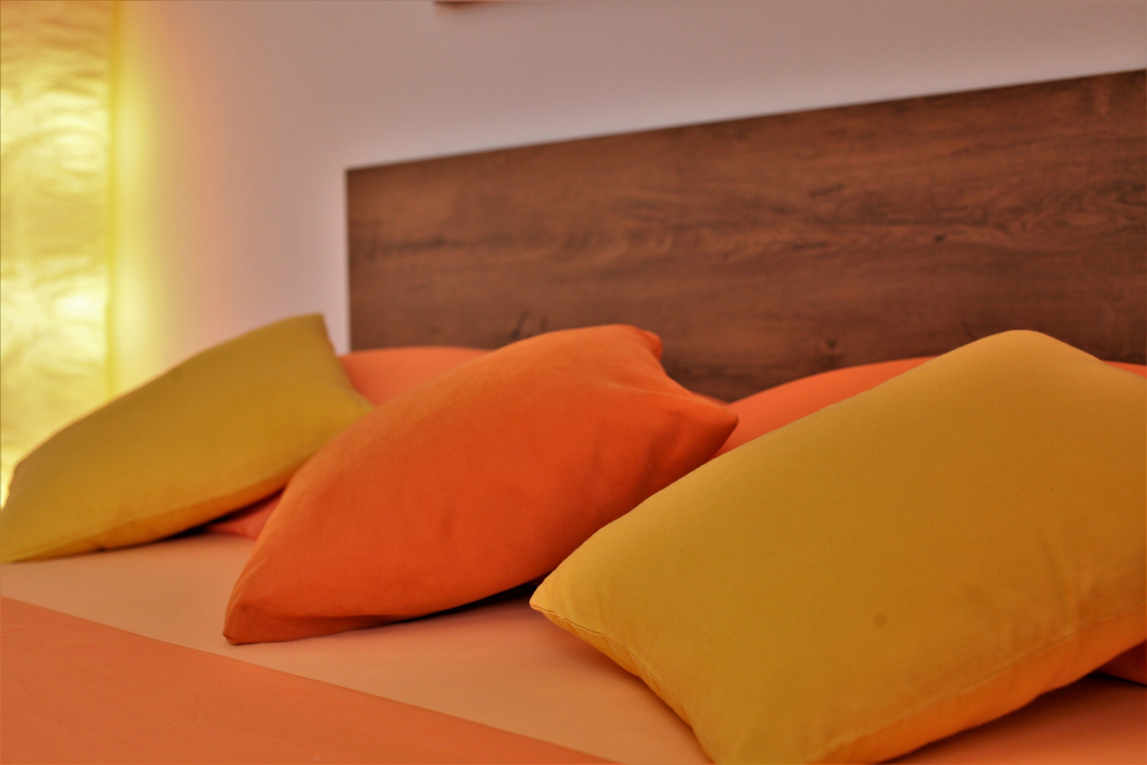 Un lit avec des oreillers orange et jaunes, une tête de lit en bois et une couvre-lit de couleur claire.