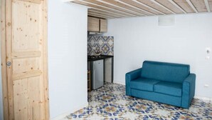 A room with a wooden door, a blue sofa, and a kitchen area with tiled flooring. - Casa Niccolò 5 (max 4 pp) (Napoli)