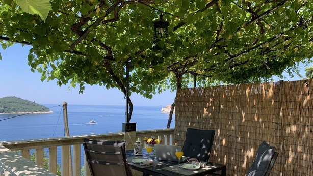 Ein Essbereich im Freien mit Tisch und Stühlen, mit Blick auf ein Gewässer und eine entfernte Insel.