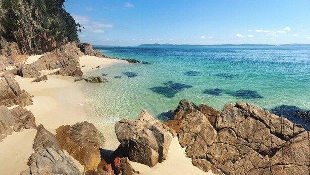 Un paisaje costero con aguas turquesas cristalinas, afloramientos rocosos y una playa arenosa.
