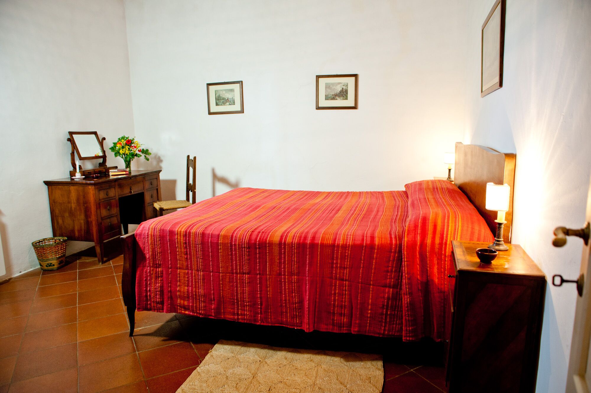 A bedroom with a bed, a nightstand, a dresser, a chair, and two framed pictures on the wall.