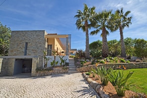 Stroll through the landscaped garden, featuring a variety of plants and shrubs, to the entrance of this modern property with a clean, functional design.