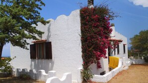 A white building with a curved white wall, a window with brown shutters, and a yellow cloth hanging on the wall. - Independent beachfront accommodation. (valledoria)