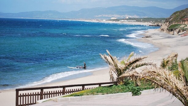 A coastal beach scene with a clear view of the ocean, a sandy shore, and a person on a surfboard. - Independent beachfront accommodation. (valledoria)